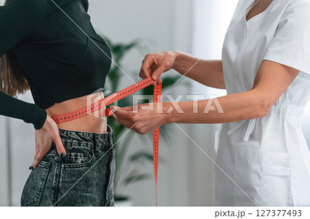 Standing and measuring the waist of customer. Young woman at a nutritionist's appointment. Medical care 127377493