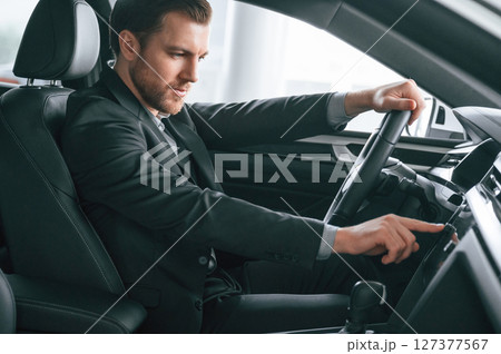 Turning the knobs. Man in formal business clothes is sitting in the modern automobile 127377567