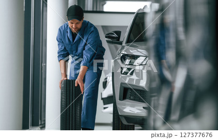 Moving the tire. Man in blue uniform is working in the car service 127377676