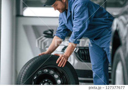 Moving the tire. Man in blue uniform is working in the car service Moving the tire. Man in blue uniform is working in the car service 127377677