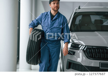 With tire in the hands. Man in blue uniform is working in the car service 127377687