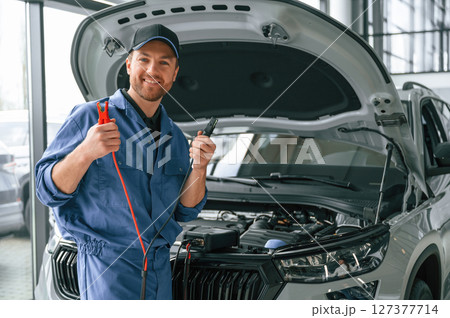 Holding the electrical terminals. Man in blue uniform is working in the car service Holding the electrical terminals. Man in blue uniform is working in the car service 127377714