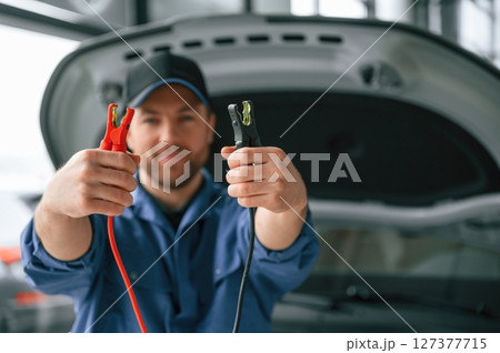 Holding the electrical terminals. Man in blue uniform is working in the car service Holding the electrical terminals. Man in blue uniform is working in the car service 127377715