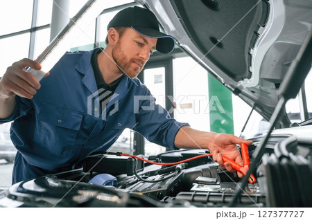 Testing breakage by using electrical terminals. Man in blue uniform is working in the car service Testing breakage by using electrical terminals. Man in blue uniform is working in the car service 127377727