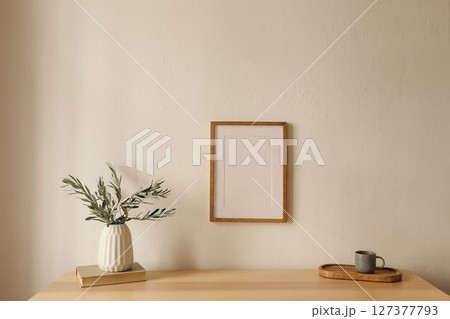 Mediterranean living room interior. Cup of coffee tea, old books on table. White wall background. Empty wooden vertical picture frame mockup hanging on white wall background. Vase with olive branches. Mediterranean living room interior. Cup of coffee tea, old books on table. White wall background. Empty wooden vertical picture frame mockup hanging on white wall background. Vase with olive branches. 127377793