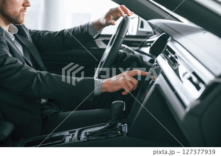 Turning the knobs. Man in formal business clothes is sitting in the modern automobile Turning the knobs. Man in formal business clothes is sitting in the modern automobile 127377939