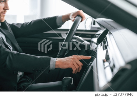 Turning the knobs. Man in formal business clothes is sitting in the modern automobile 127377940