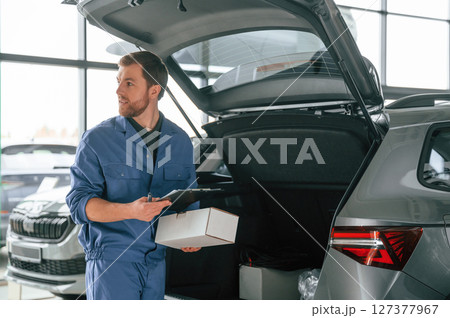 White box and notepad in hands. Man in blue uniform is working in the car service White box and notepad in hands. Man in blue uniform is working in the car service 127377967