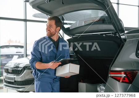 White box and notepad in hands. Man in blue uniform is working in the car service 127377968