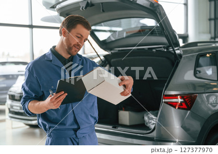 With box and notepad. Man in blue uniform is working in the car service 127377970