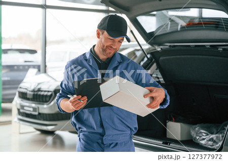 With box and notepad. Man in blue uniform is working in the car service 127377972