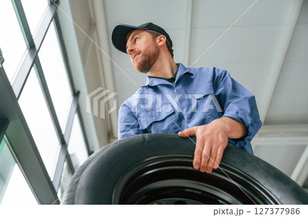 View from below. Holding tire. Man in blue uniform is working in the car service View from below. Holding tire. Man in blue uniform is working in the car service 127377986