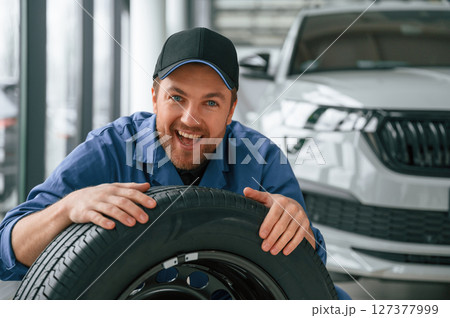 New tire. Leaning on it. Man in blue uniform is working in the car service 127377999