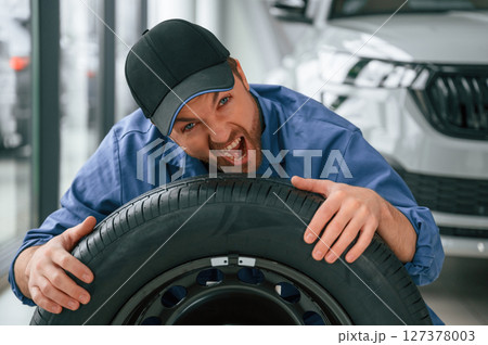 Having fun, smiling, with tire. Man in blue uniform is working in the car service Having fun, smiling, with tire. Man in blue uniform is working in the car service 127378003
