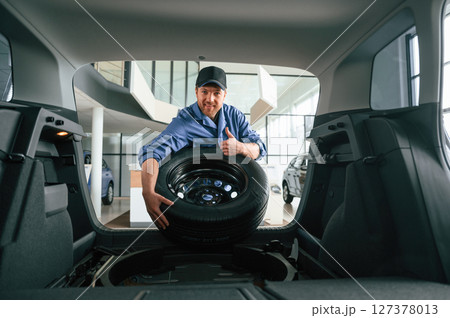 Putting the tire out of automobile. Man in blue uniform is working in the car service Putting the tire out of automobile. Man in blue uniform is working in the car service 127378013