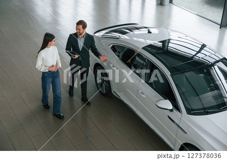 Talking, holding tablet. Man is showing the new automobile to the woman customer in the car dealership 127378036