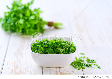 Chopped fresh parsley in a ceramic bowl on a white table, selective focus. 127378060
