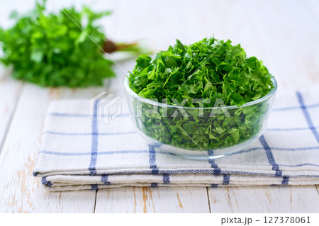 Chopped fresh parsley in a clear glass bowl on a white table, selective focus. 127378061