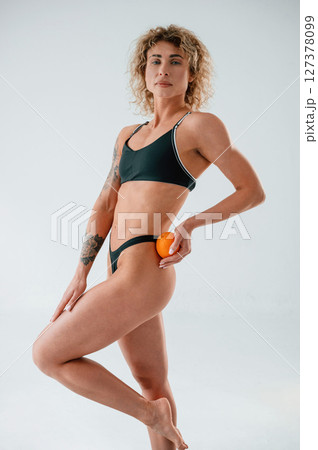 Holding orange fruit. Young caucasian woman with athletic body shape is indoors at daytime 127378099