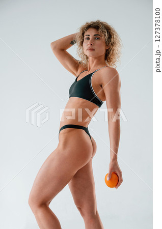 Holding orange fruit. Young caucasian woman with athletic body shape is indoors at daytime Holding orange fruit. Young caucasian woman with athletic body shape is indoors at daytime 127378100