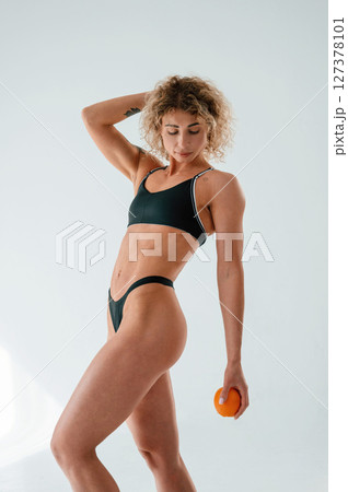 Holding orange fruit. Young caucasian woman with athletic body shape is indoors at daytime Holding orange fruit. Young caucasian woman with athletic body shape is indoors at daytime 127378101