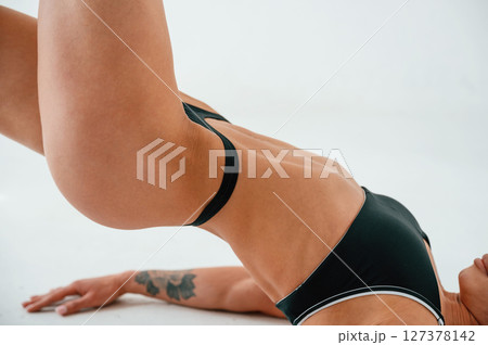 Side view. Lying down on the floor. Young caucasian woman with athletic body shape is indoors at daytime 127378142