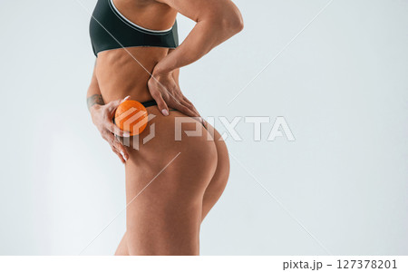 Orange fruit in hand, close up view. Young caucasian woman with athletic body shape is indoors at daytime Orange fruit in hand, close up view. Young caucasian woman with athletic body shape is indoors at daytime 127378201