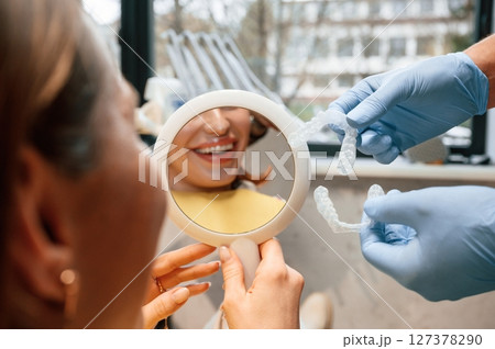 Using mirror to look at aligner on teeth. Woman in the stomatology clinic, visiting dentist Using mirror to look at aligner on teeth. Woman in the stomatology clinic, visiting dentist 127378290