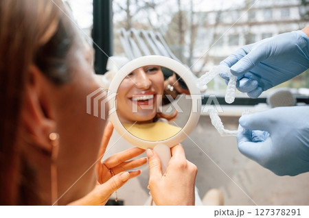 Using mirror to look at aligner on teeth. Woman in the stomatology clinic, visiting dentist Using mirror to look at aligner on teeth. Woman in the stomatology clinic, visiting dentist 127378291