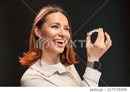 Young woman is standing against black background and holding aligner Young woman is standing against black background and holding aligner 127378300