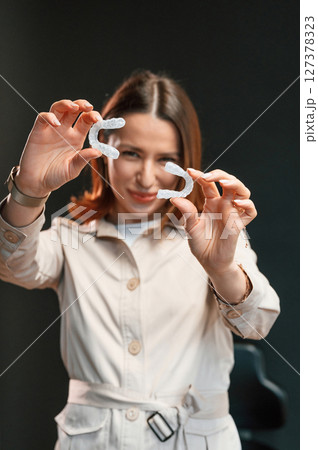 Holding two aligners. Young woman is standing against black background and holding 127378323