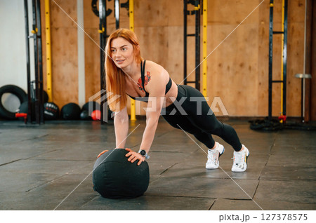 Doing push ups by using soft ball. Beautiful strong woman is in the gym 127378575