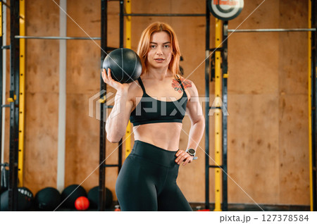 Holding ball. Beautiful strong woman is in the gym 127378584