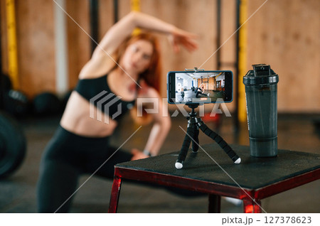 Shooting video by smartphone. Doing exercises. Beautiful strong woman is in the gym 127378623