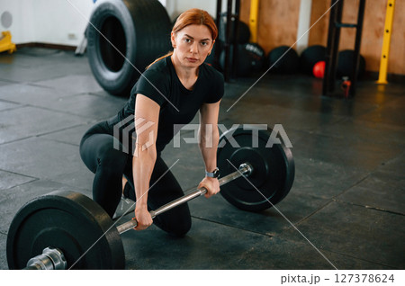 Leaning on the barbell. On the floor. Beautiful strong woman is in the gym Leaning on the barbell. On the floor. Beautiful strong woman is in the gym 127378624