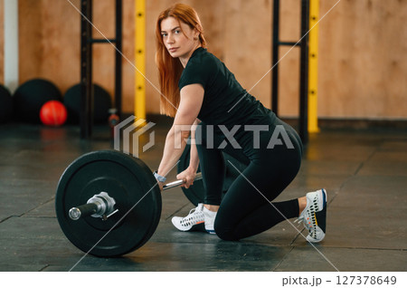 Sitting with barbell on the floor. Beautiful strong woman is in the gym 127378649