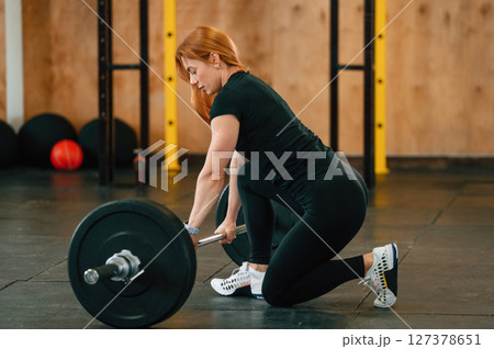 View from the side. Sitting with barbell on the floor. Beautiful strong woman is in the gym 127378651