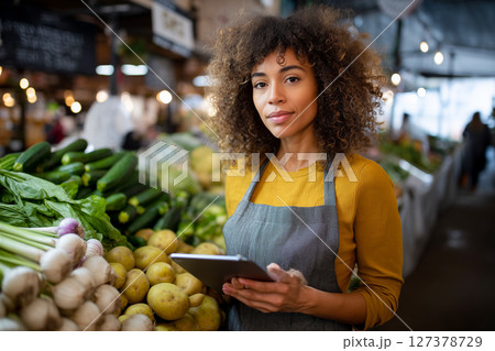 A woman stands in a produce market with a tablet in her hand 127378729