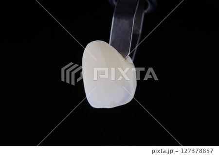 Close up shot ultra thin dental zirconium crown is held with tweezers with black background. 127378857