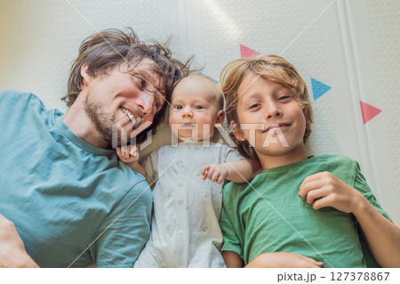 Father, son, and newborn baby lying on the floor in a cozy nursery, celebrating the arrival of their newest family member. Parenthood, bonding, and family love concept Father, son, and newborn baby lying on the floor in a cozy nursery, celebrating the arrival of their newest family member. Parenthood, bonding, and family love concept 127378867