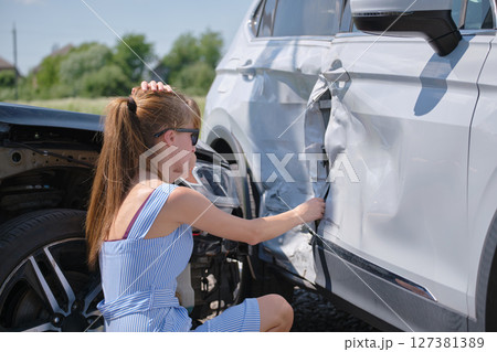 Sad young woman driver sitting near her smashed car looking shocked on crashed vehicles in road accident Sad young woman driver sitting near her smashed car looking shocked on crashed vehicles in road accident 127381389