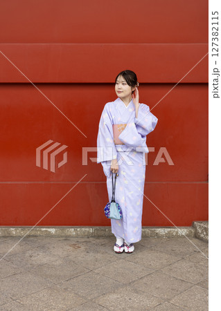 神社の朱色の壁の前に立つ和装の日本人女性 127382115