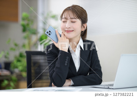 スマホを持つディスクワーク中の若いビジネスウーマン  127382221