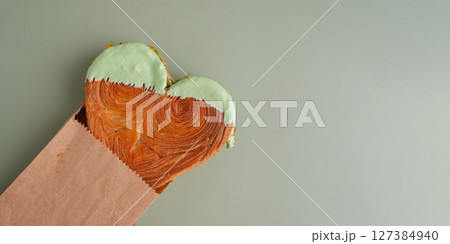 Heart shaped pistachio croissant delivery take away to go food on green background with copy space. Puff pastry trendy sweet dessert bakery. Creamy dough experiment Heart shaped pistachio croissant delivery take away to go food on green background with copy space. Puff pastry trendy sweet dessert bakery. Creamy dough experiment 127384940