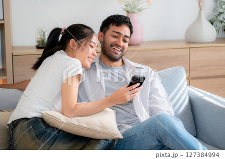 Young asian couple relax sitting on sofa looking smartphone together in living room. Young asian couple relax sitting on sofa looking smartphone together in living room. 127384994