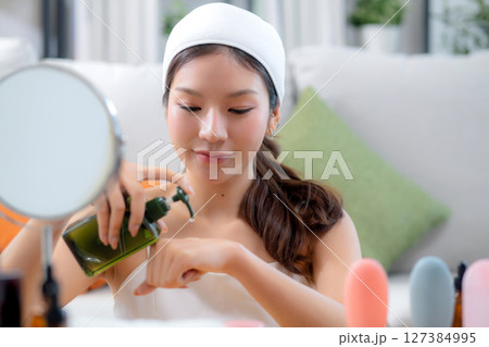 Beautiful young asian woman applying lotion herb on hands looking mirror at home. Beautiful young asian woman applying lotion herb on hands looking mirror at home. 127384995