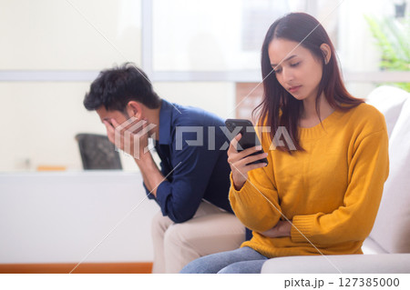 Unhappy asian couple sitting on sofa having relationship problem in living room at home. 127385000
