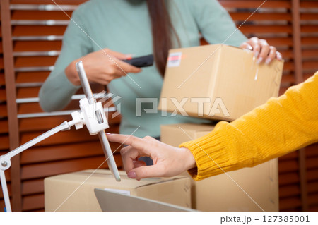 Closeup hand woman live online while scanning package with barcode reader in office. 127385001