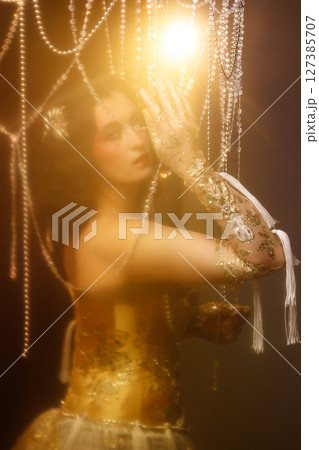 Young woman in vintage corset costume posing under chandelier on dark background 127385707