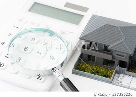 電卓と虫眼鏡とミニチュアの一戸建て住宅 127386226
